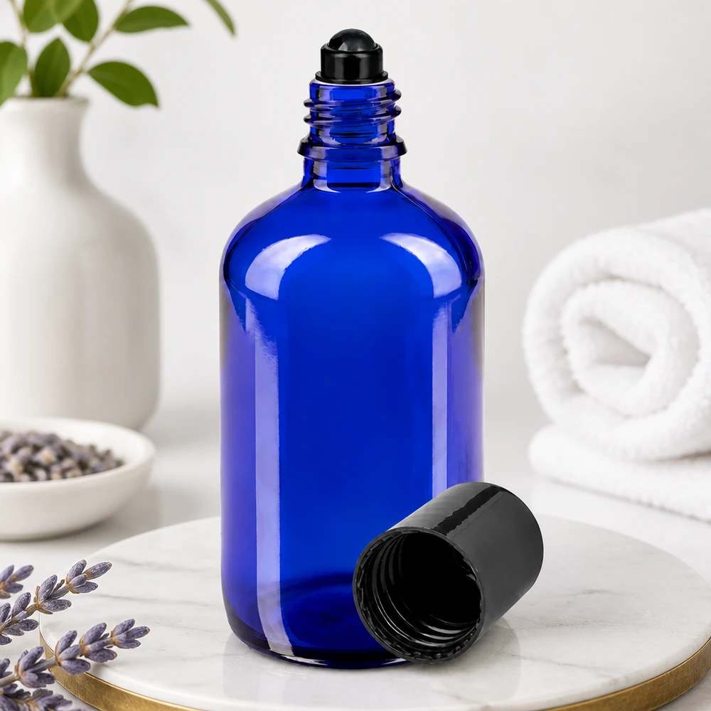 Frasco de vidro azul de 100 ml com bola rolante preta e tampa removida sobre mármore
