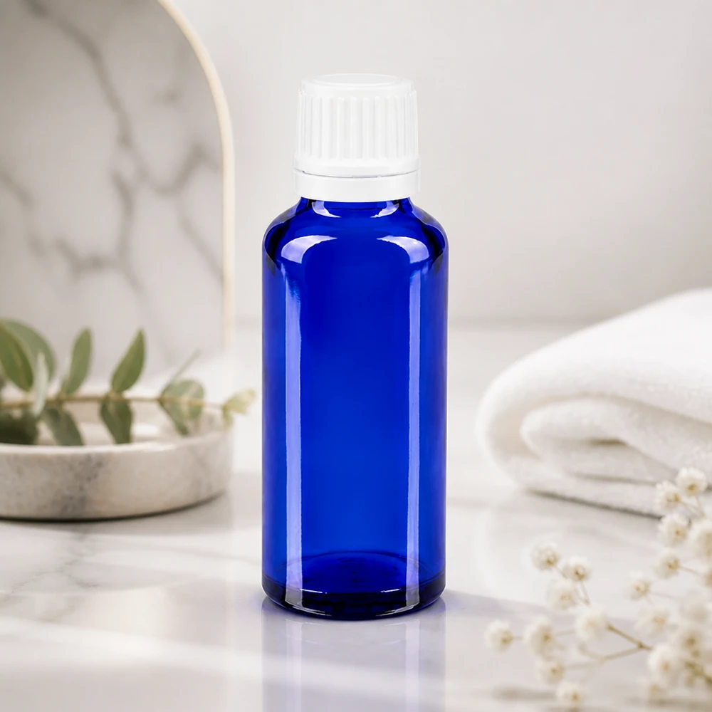 Frasco de farmácia azul de 30 ml com conta-gotas de 0,7 mm sobre mármore branco, ao lado de uma toalha dobrada