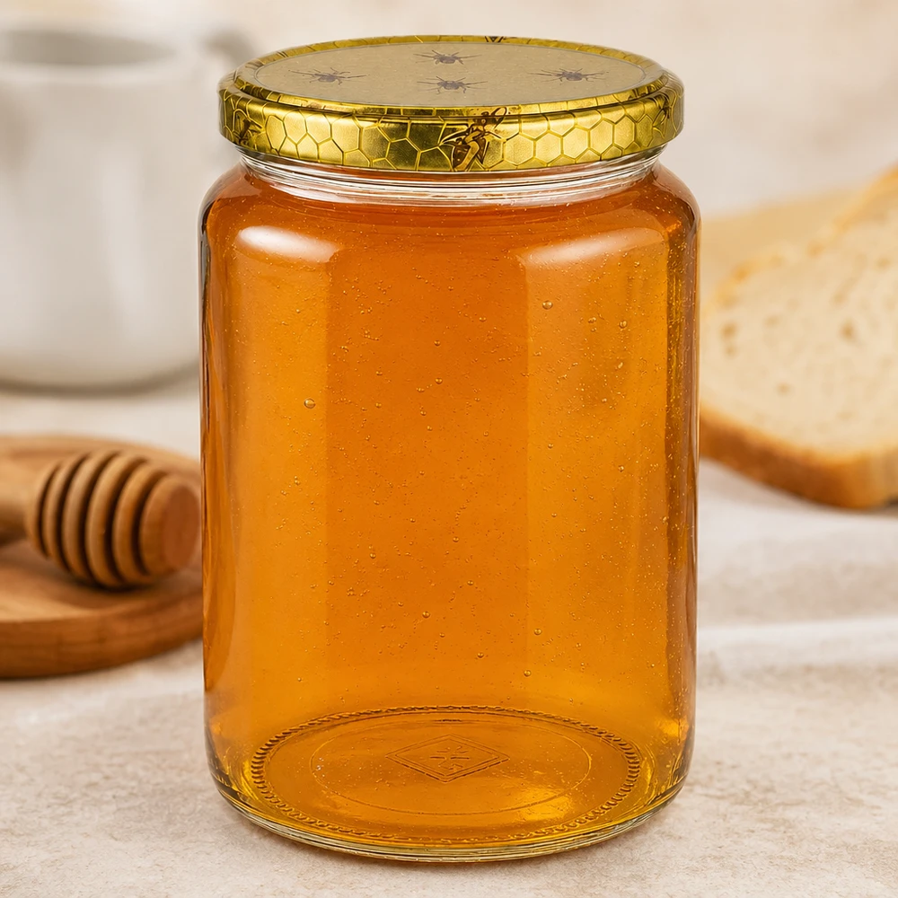 1000g Honigglas mit Bienenwabe Deckel BasicSeal UNiTWIST Frasco de mel grande de 1000 g com relevo no fundo, ao lado de um pau de mel e de pão numa tábua de madeira Cenário de cozinha Material de apicultura