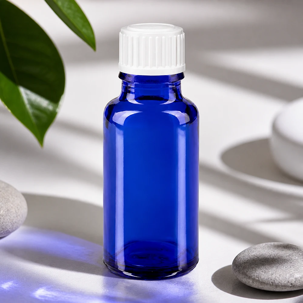 Frasco de vidro azul de 20 ml com tampa branca, ao lado de pedras naturais e folhas verdes