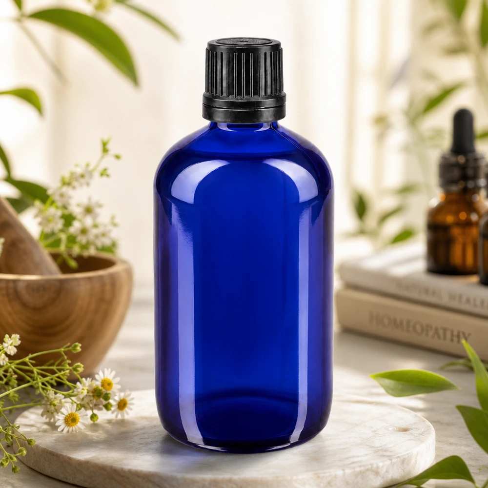 Frasco de vidro de farmácia azul de 100 ml com tampa preta estriada, entre flores de camomila e ervas medicinais