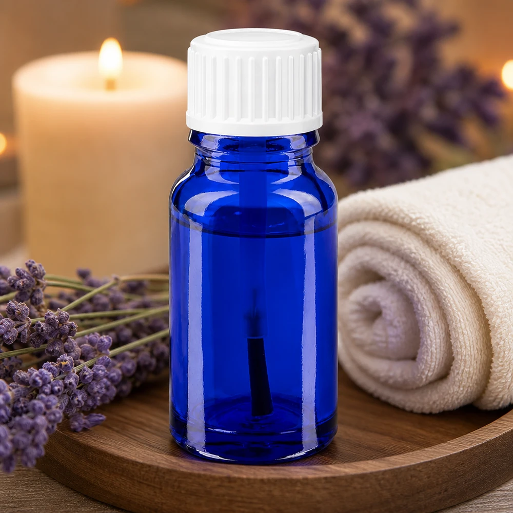 Frasco de aromaterapia de 10 ml em vidro azul de farmácia com bico de pincel branco ao lado de flores de lavanda