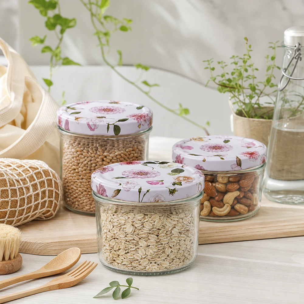 Frasco cilíndrico de 230 ml + tampa BasicSeal cor-de-rosa Três frascos cilíndricos de 230 ml com tampas de flores cor-de-rosa cheios de cereais e frutos secos num ambiente de cozinha sustentável