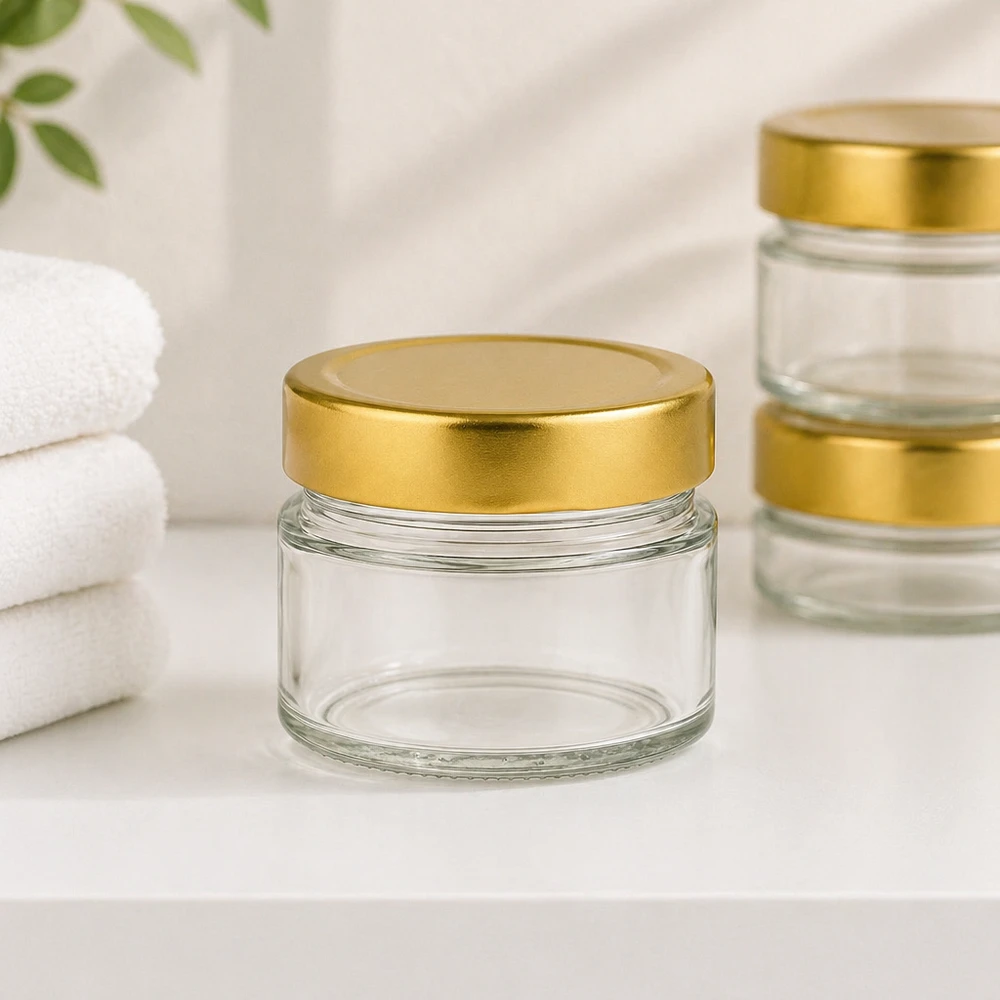 Frasco redondo de 80 ml com tampa BasicSeal dourada num ambiente de casa de banho com toalhas brancas para cosméticos