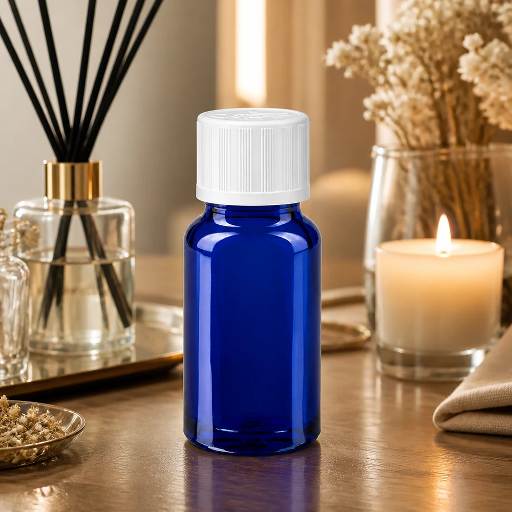 Pequeno frasco de vidro azul de 10 ml com tampa de rosca branca, em cima de uma mesa de madeira, ao lado de um difusor de aroma e de uma vela