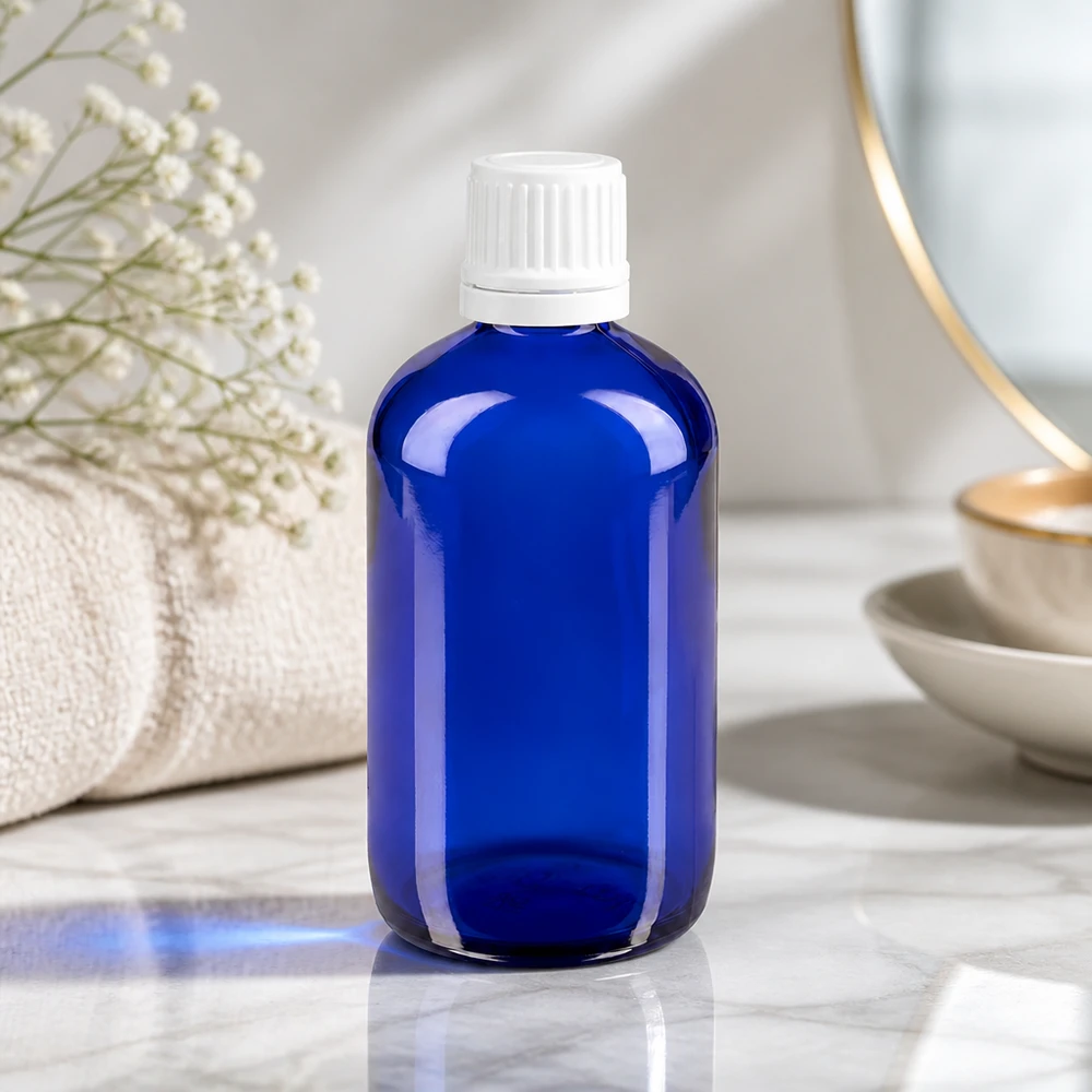 Frasco de farmácia azul 100ml tampa de rosca branca fecho inviolável Garrafa de vidro azul de 100 ml com tampa OV branca sobre mármore, ao lado de uma toalha e de flores secas