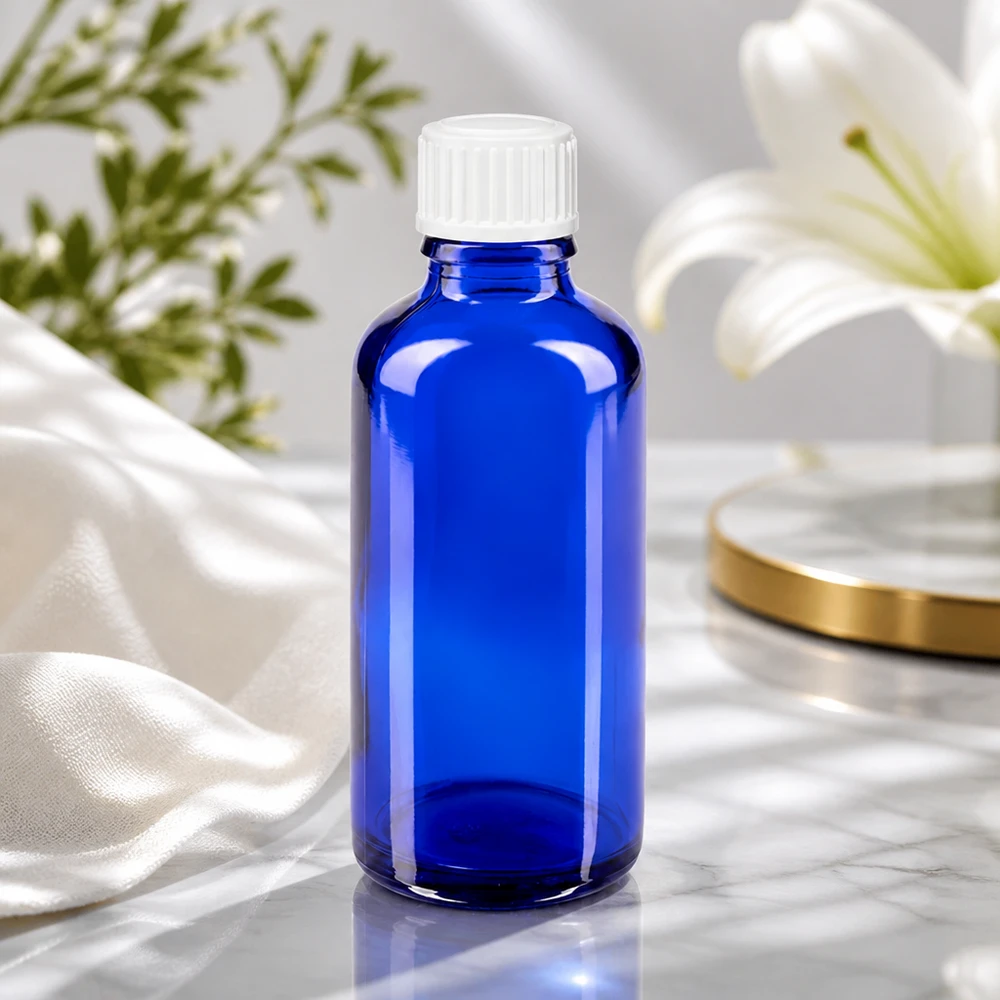 Frasco de vidro azul de 50 ml com tampa de rosca branca ao lado de um lírio branco sobre uma superfície de mármore