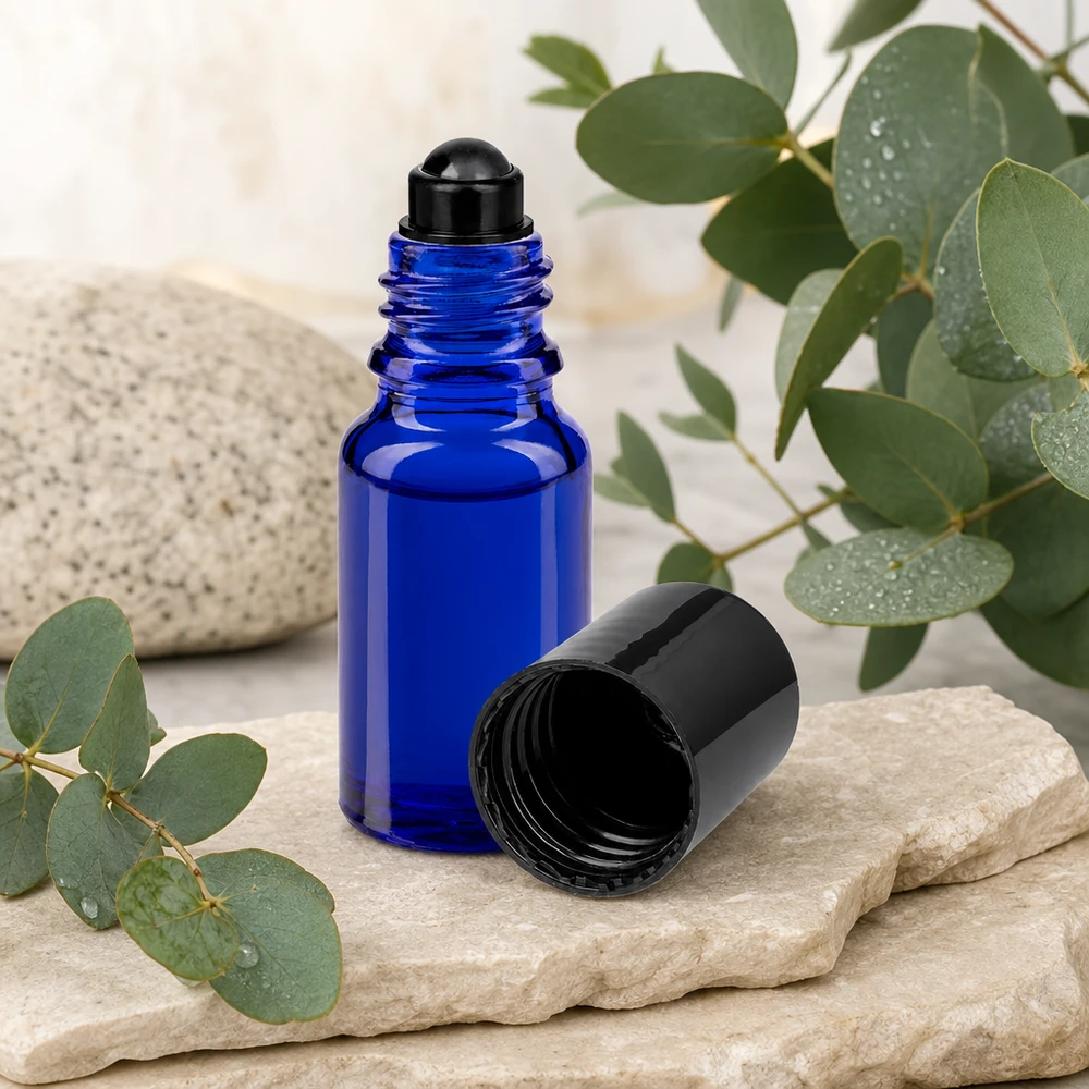 Frasco de farmácia azul 10ml tampa roll-on preta Frasco roll-on ApoGlas azul de 10 ml com tampa preta, ao lado de ramos de eucalipto sobre pedra natural