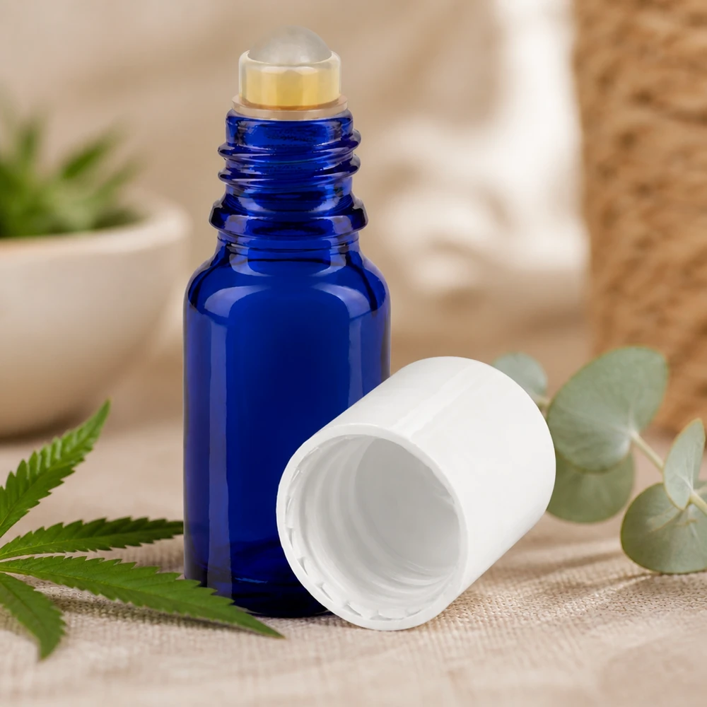 Frasco azul de 10 ml com aplicador de rolo e tampa branca, ao lado de folhas de cânhamo e eucalipto sobre tecido de linho