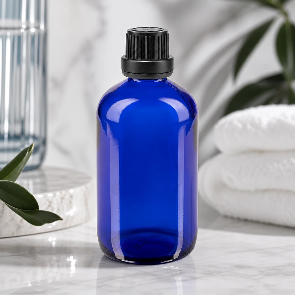 Garrafa de vidro azul de 100 ml com tampa preta estriada, ao lado de toalhas brancas e plantas verdes