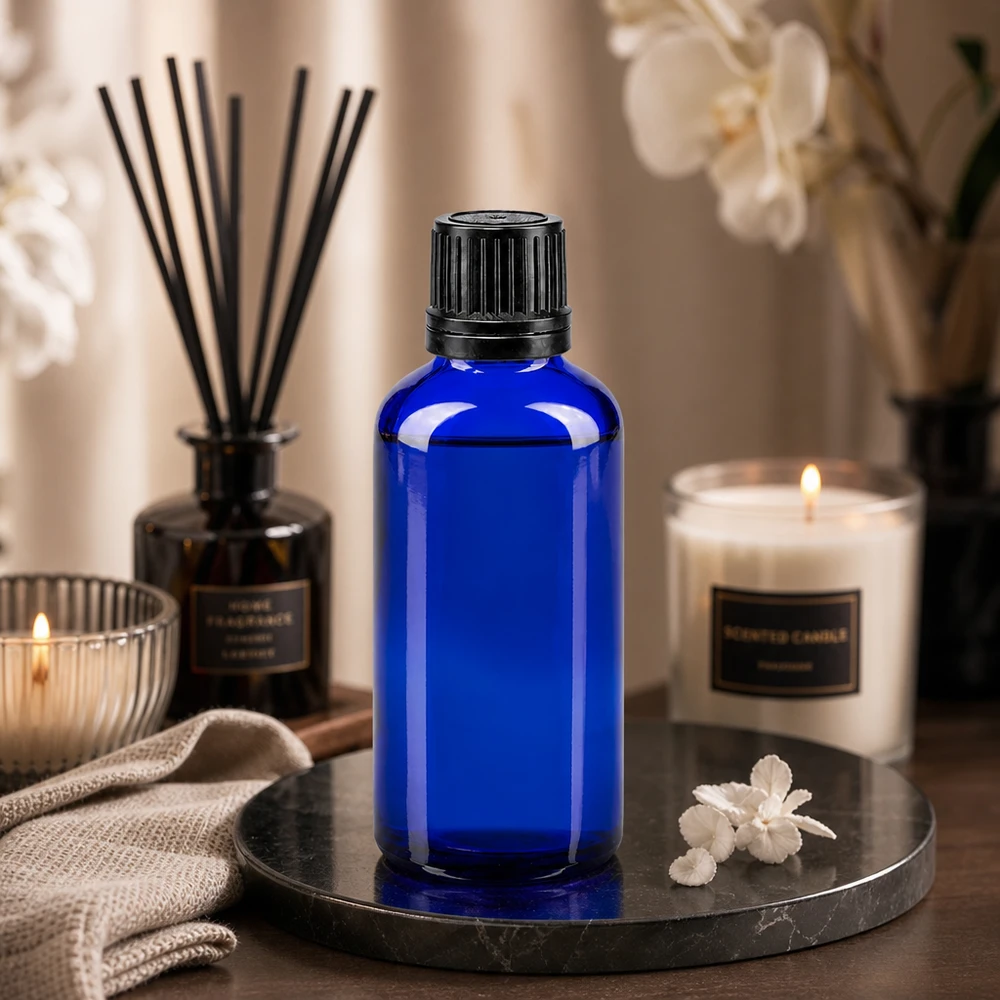 Frasco de vidro azul de 50 ml com tampa de rosca preta, sobre uma bandeja de mármore com velas e difusor de aroma
