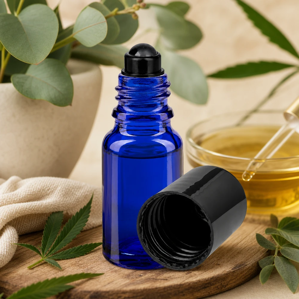 Frasco roll-on ApoGlas azul de 10 ml com tampa preta, sobre uma tábua de madeira, ao lado de uma folha de canábis e de um ramo de eucalipto