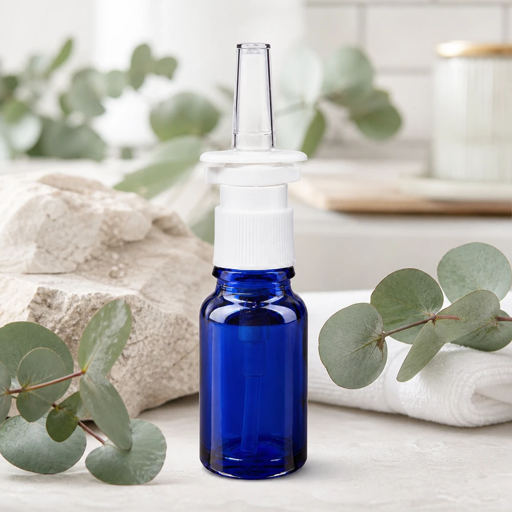 Frasco de vidro azul de 10 ml com bico pulverizador nasal transparente, sobre um fundo natural de eucalipto