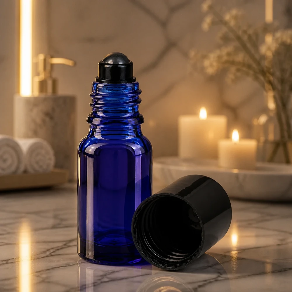 Frasco roll-on azul cobalto de 10 ml com esferinha preta, à luz evocativa de uma vela sobre mármore