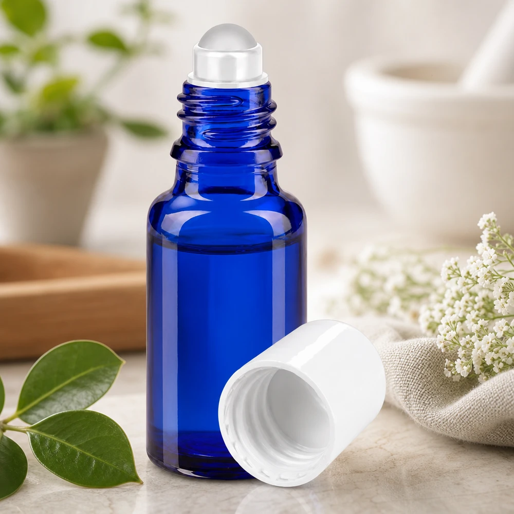 Frasco de farmácia azul 20ml tampa roll-on branca Frasco de vidro de farmácia azul de 20 ml com uma esfera rolante transparente, ao lado de flores brancas e folhas verdes