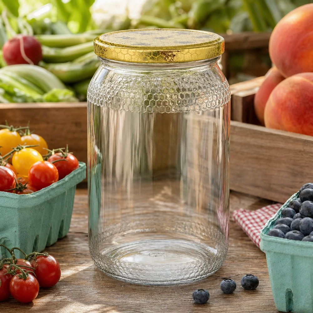 Frasco de mel de 900 ml vazio com tampa dourada em forma de favo de mel entre frutos e legumes frescos numa mesa de cozinha de madeira