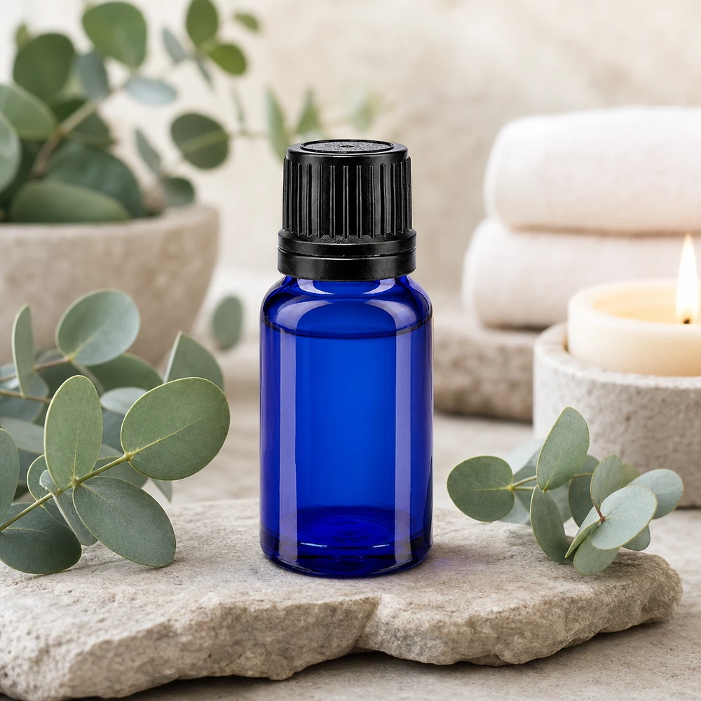 Frasco conta-gotas azul de 10 ml com tampa de rosca preta, apoiado sobre pedra natural com ramos de eucalipto
