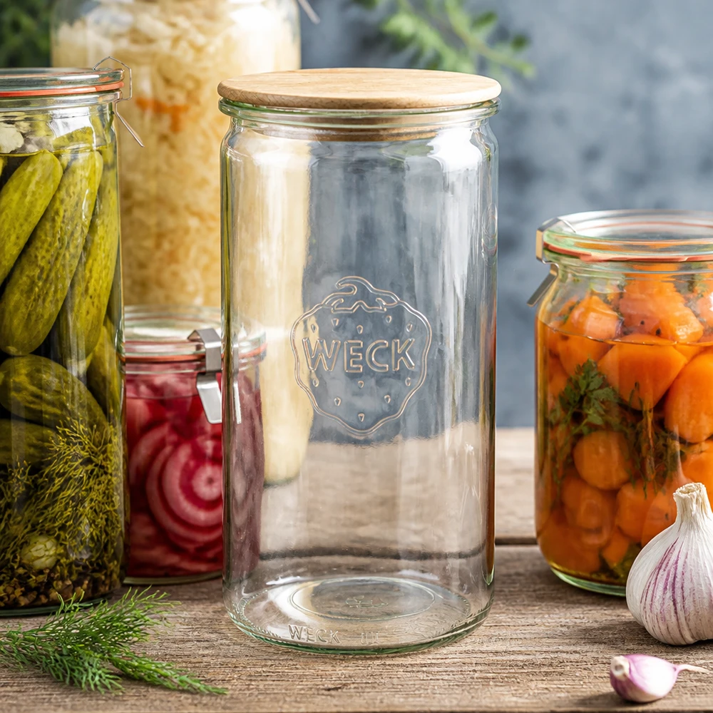 WECK Zylinderglas 1590ml RR100 mit Holzdeckel zwischen Einmachgläsern mit Gurken Karotten und Sauerkraut auf Holztisch