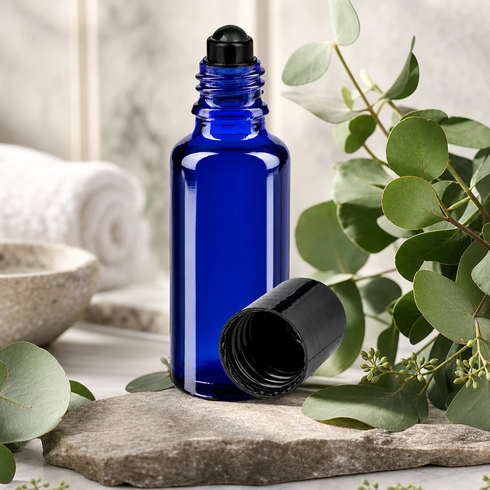 Frasco de farmácia azul 30ml com tampa de rosca preta Frasco de vidro azul cobalto de 30 ml com aplicador roll-on preto sobre uma pedra natural, entre ramos de eucalipto