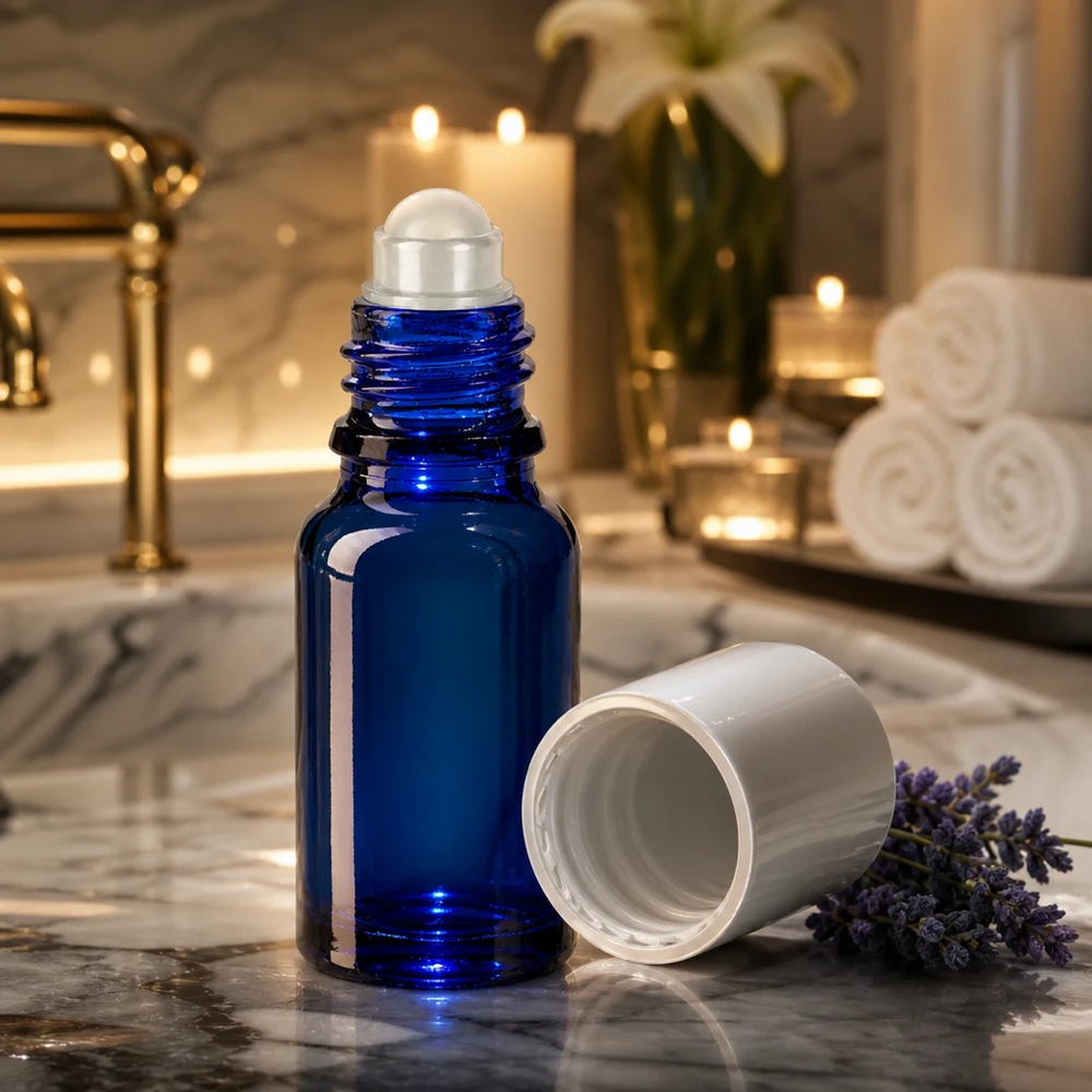 Frasco roll-on azul cobalto de 10 ml com aplicador de esfera rolante sobre mármore, ao lado de flores de lavanda