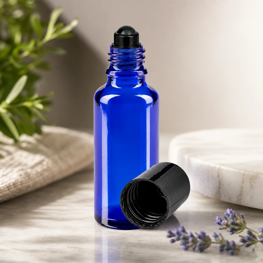 Frasco de farmácia azul 30ml com tampa de rosca preta Frasco de vidro azul cobalto de 30 ml com aplicador roll-on e tampa preta, ao lado de um ramo de lavanda e de alecrim