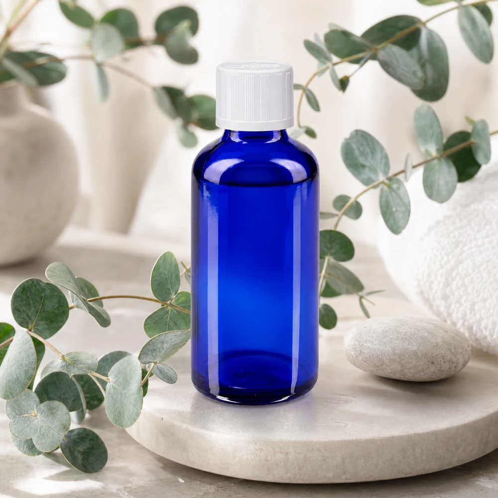 Frasco de farmácia azul de 50 ml com tampa de segurança branca, sobre uma bandeja de mármore com eucalipto
