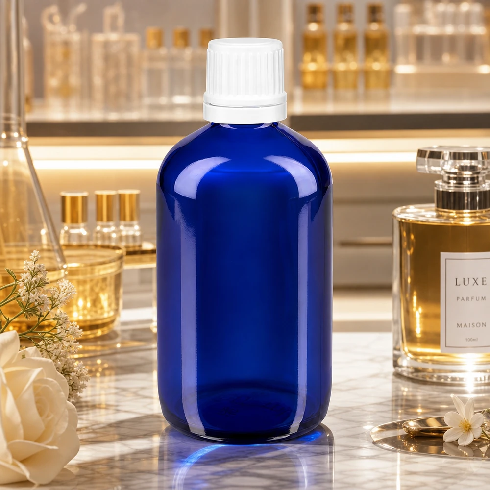 Frasco de farmácia azul 100ml tampa de rosca branca fecho inviolável Frasco de vidro azul de farmácia de 100 ml com tampa OV branca de 11 mm sobre mármore, ao lado de um perfume de luxo