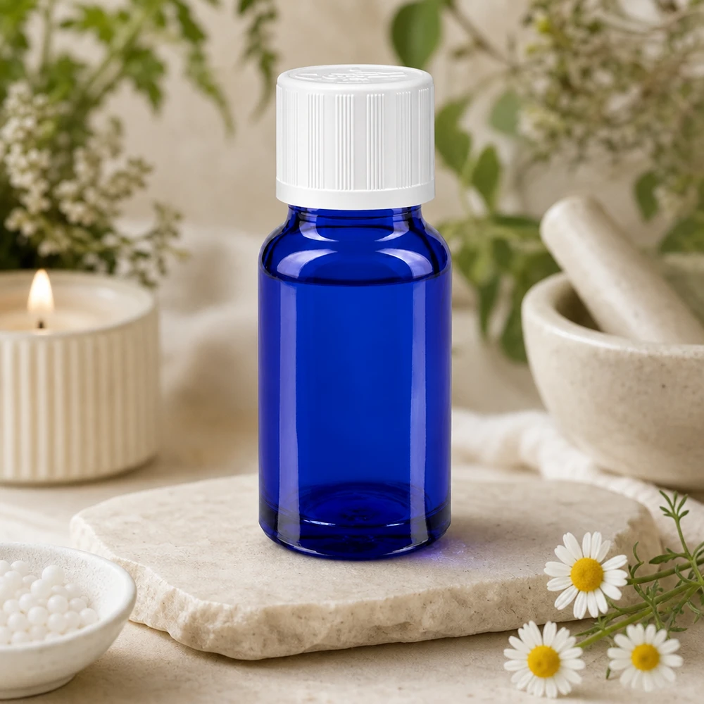 Frasco de farmácia azul de 10 ml com tampa KiSi branca sobre uma placa de pedra, ao lado de flores de camomila