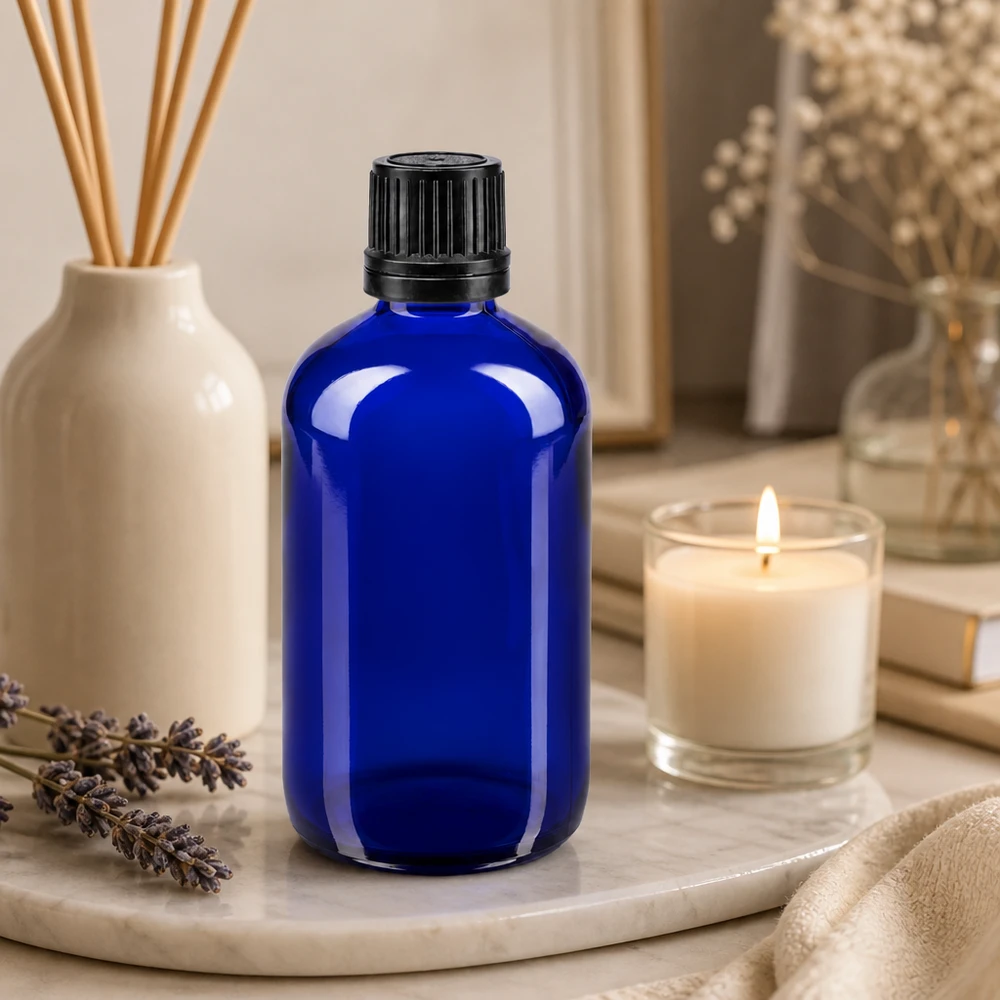 Frasco de vidro azul de 100 ml com tampa conta-gotas preta, sobre uma bandeja de mármore com lavanda e uma vela