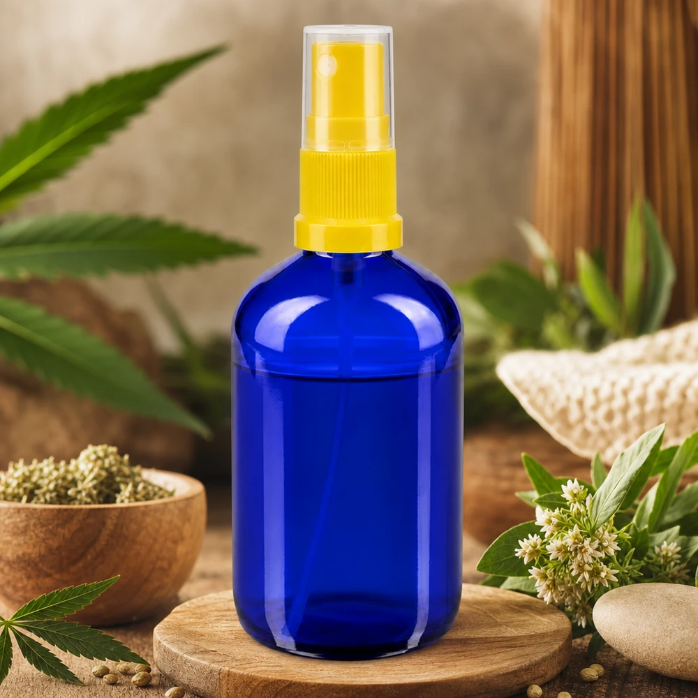 Frasco de vidro azul de 100 ml com pulverizador amarelo, rodeado por uma planta de cânhamo e ervas naturais