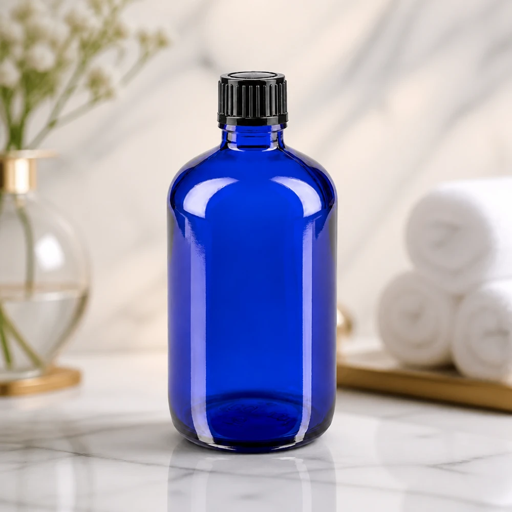 Frasco cilíndrico de vidro azul de 100 ml com tampa de rosca preta estriada sobre uma superfície de mármore