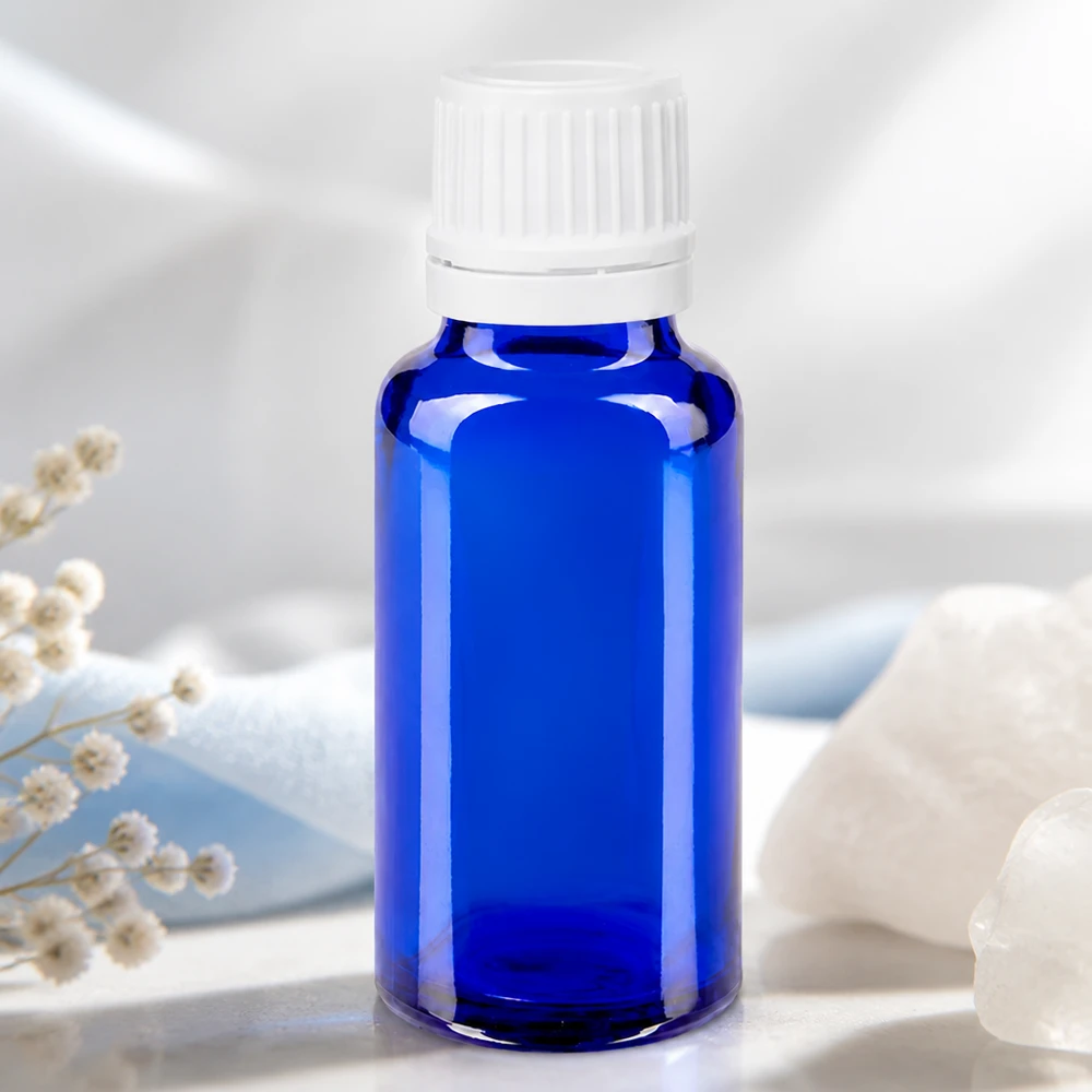 Frasco de farmácia azul cobalto de 20 ml com tampa de segurança branca, ao lado de cristal de montanha e flores secas