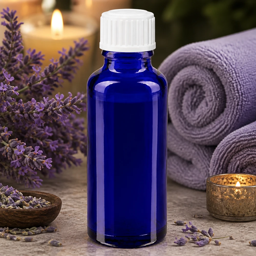 Frasco de vidro azul de 30 ml com conta-gotas branco de 3 mm, rodeado por flores de lavanda e acessórios de spa