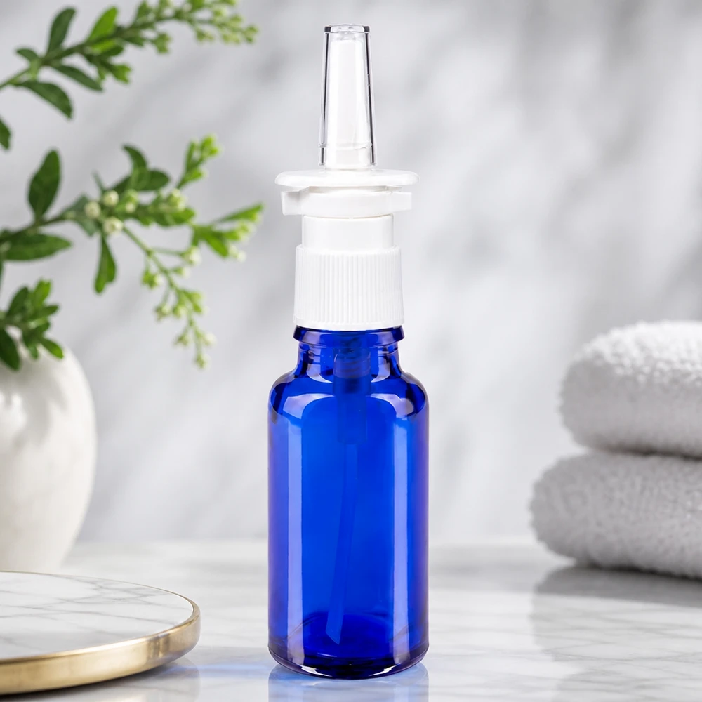 Frasco de vidro de farmácia azul de 20 ml com bico transparente para spray nasal e cabeça de pressão branca sobre fundo de mármore
