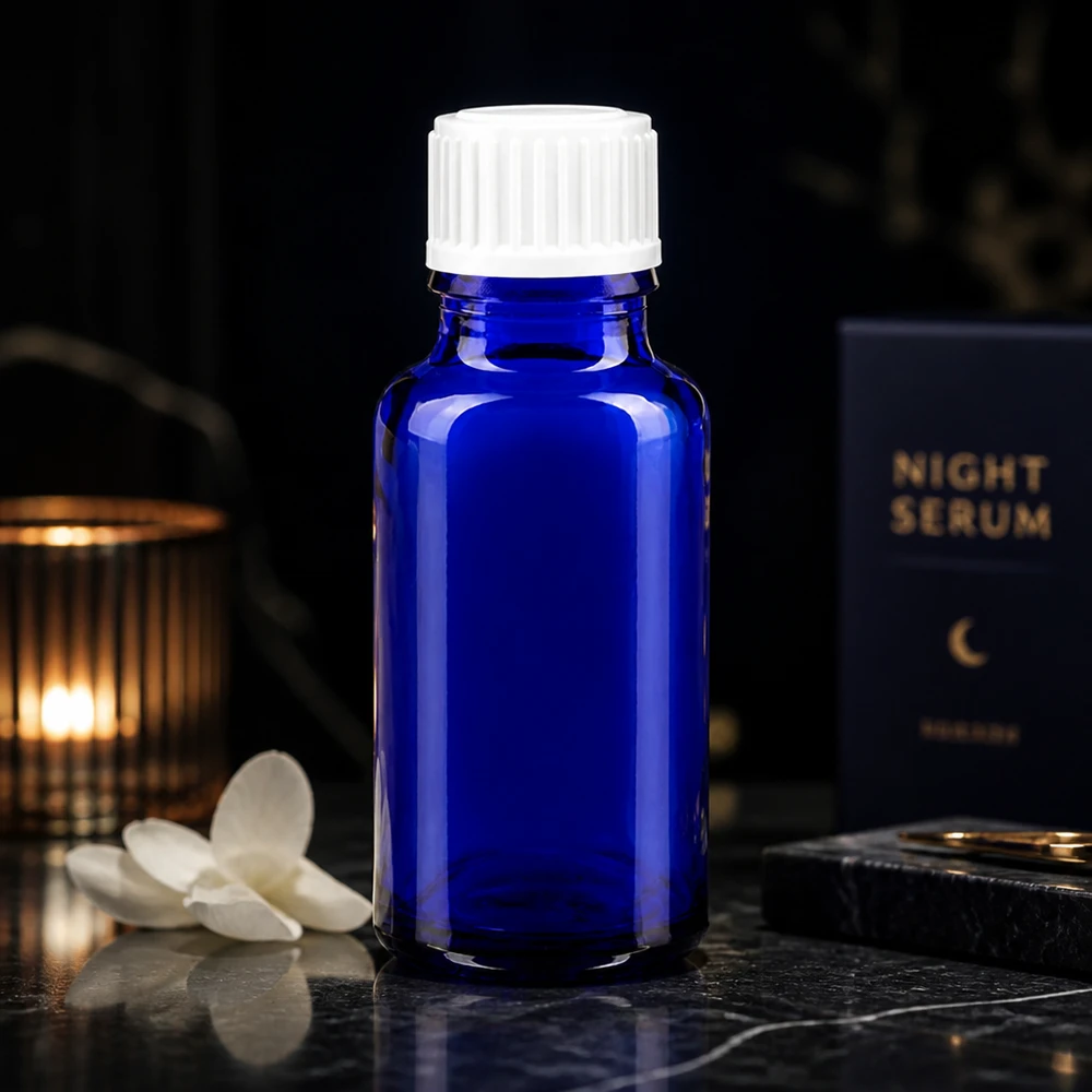 Frasco de farmácia azul 20ml tampa de rosca branco standard Frasco de vidro azul cobalto de 20 ml com tampa branca ao lado da embalagem do Night Serum sobre um fundo escuro