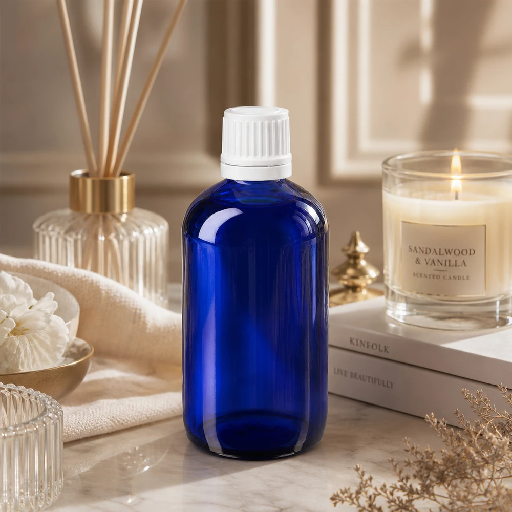 Frasco de farmácia azul 100ml tampa de rosca branca fecho inviolável Frasco de farmácia azul de vidro com 100 ml e tampa branca com fecho de segurança para crianças, sobre mármore, ao lado de uma vela de sândalo
