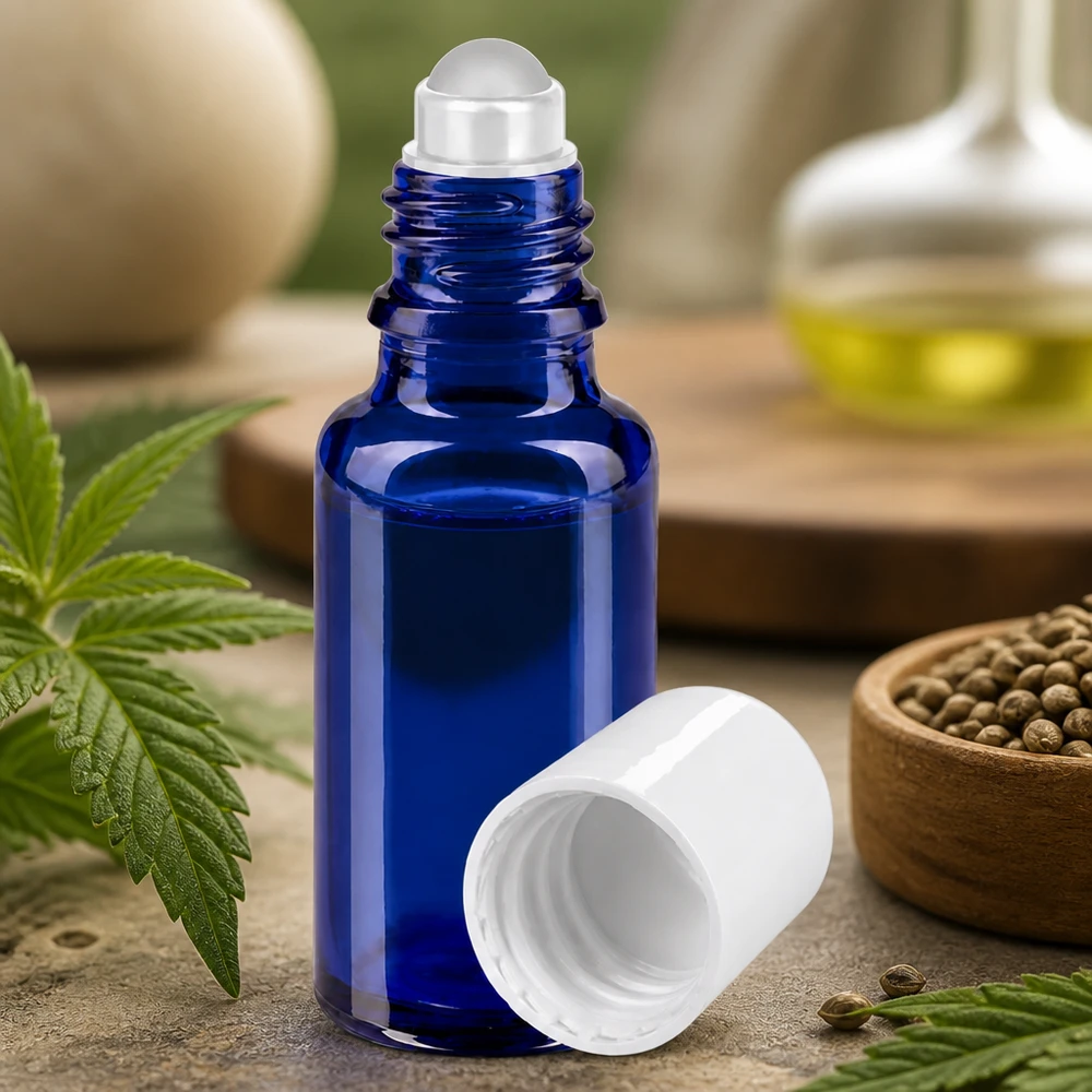 Frasco de vidro azul de 20 ml com aplicador de bola rolante e tampa branca, entre folhas e sementes de cânhamo