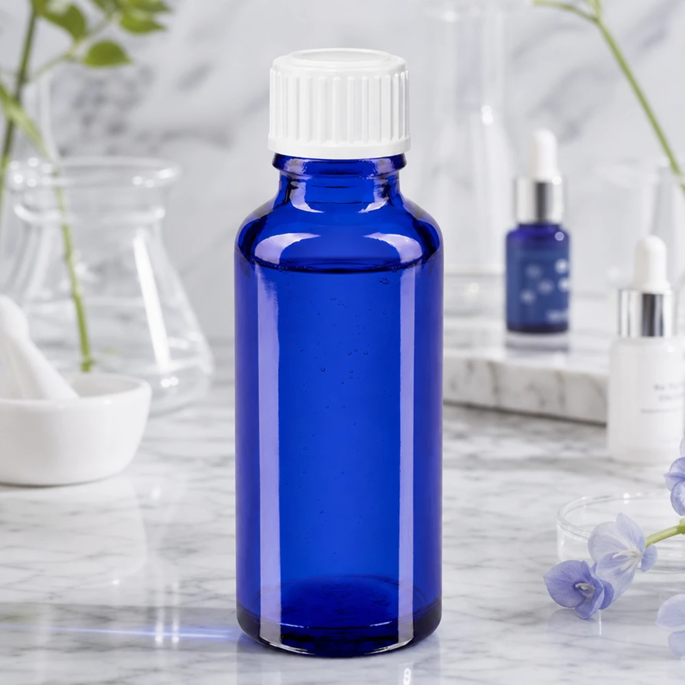 Frasco cilíndrico de vidro farmacêutico de 30 ml, em azul cobalto, com tampa de rosca branca sobre fundo marmorizado