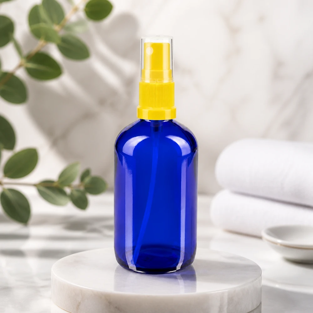 Frasco redondo azul de 100 ml, em vidro de farmácia, com pulverizador amarelo acionado com o dedo, sobre uma base de mármore