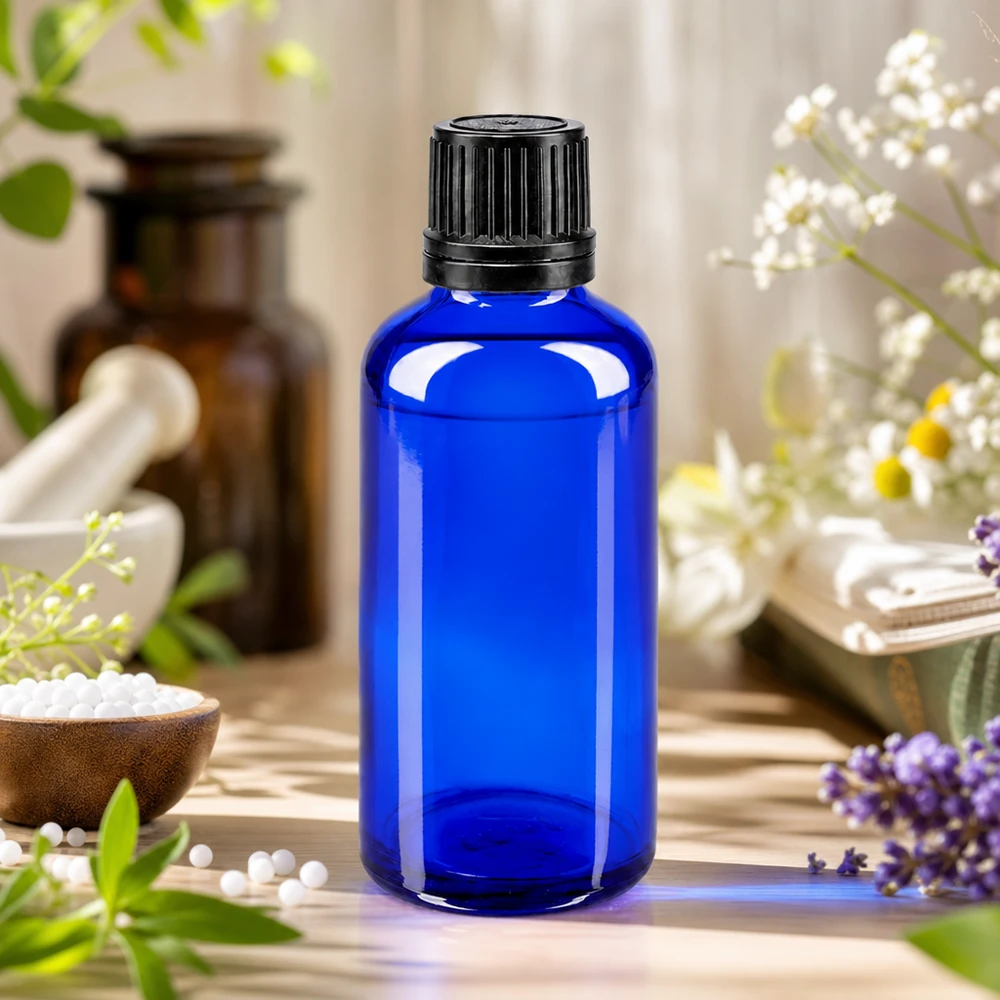 Frasco de farmácia azul de 50 ml com tampa original preta, rodeado por flores de lavanda e camomila