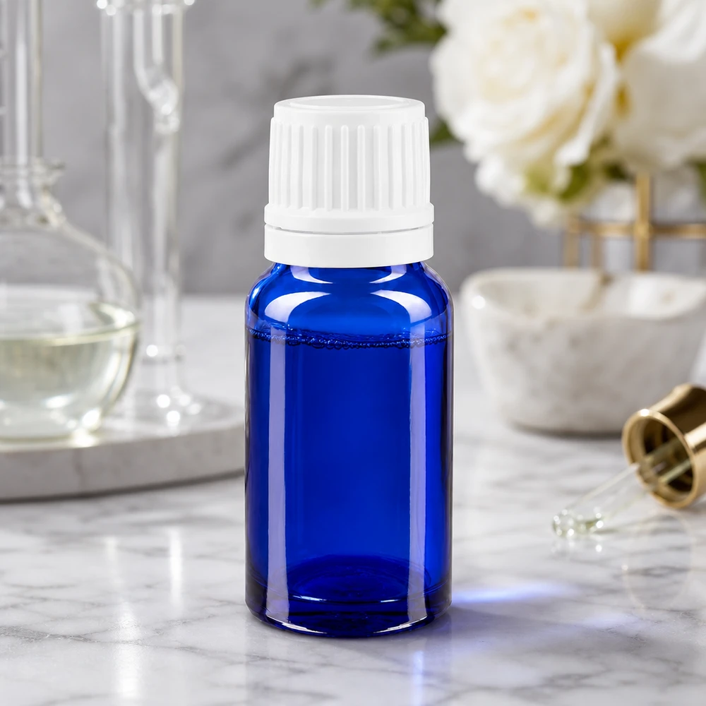 Frasco de farmácia azul 10ml conta-gotas tampa 1.2mm branca inviolável Frasco de farmácia de 10 ml, de vidro azul com tampa conta-gotas branca, sobre uma superfície de mármore, ao lado de rosas