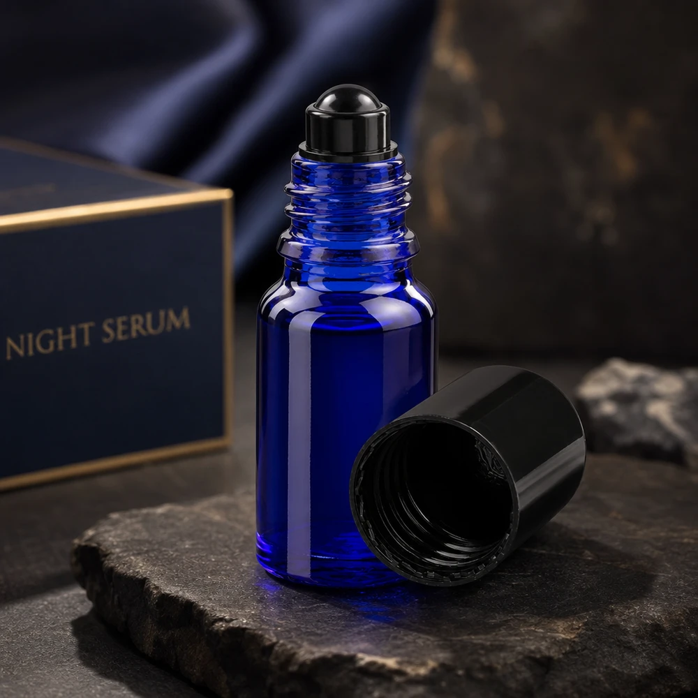 Frasco de farmácia azul 10ml tampa roll-on preta Frasco roll-on ApoGlas azul-escuro de 10 ml com tampa preta aberta sobre uma pedra de ardósia, em frente à caixa do Night Serum