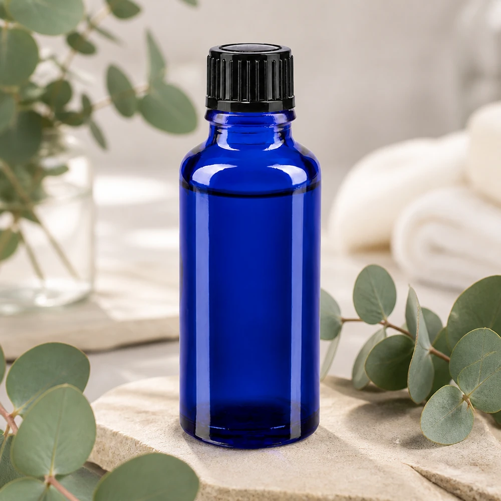 Frasco de vidro azul cobalto de 30 ml com tampa dosadora preta, apoiado sobre pedra natural com ramos de eucalipto